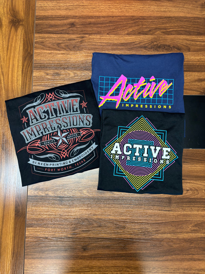 Three Active Impressions t shirts with custom designs echoing Fort Worth western style, 1980s neon pop, and geometric brights. All screen printed by the team at Active Impressions in Fort Worth, TExas